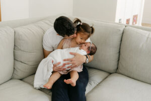 a dad with a sibling and a newborn on his lap on a couch