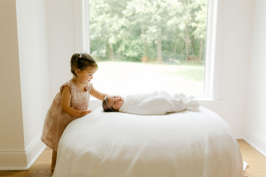 baby girl lying on a pouf with a toddler girl looking at her