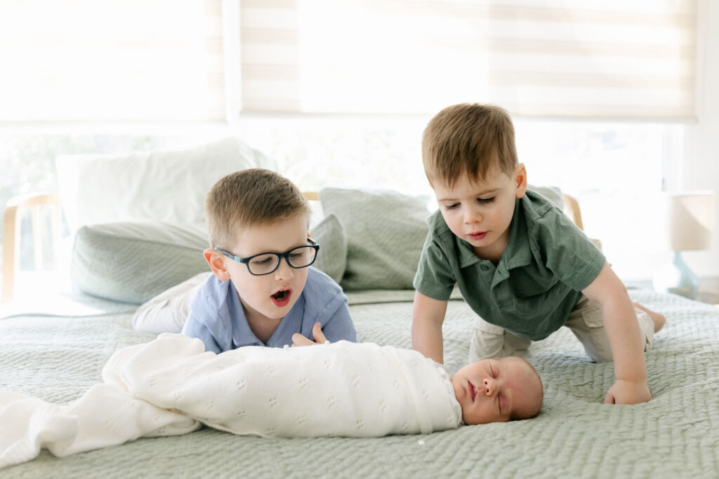 big brothers on a bed looking at a newborn brother