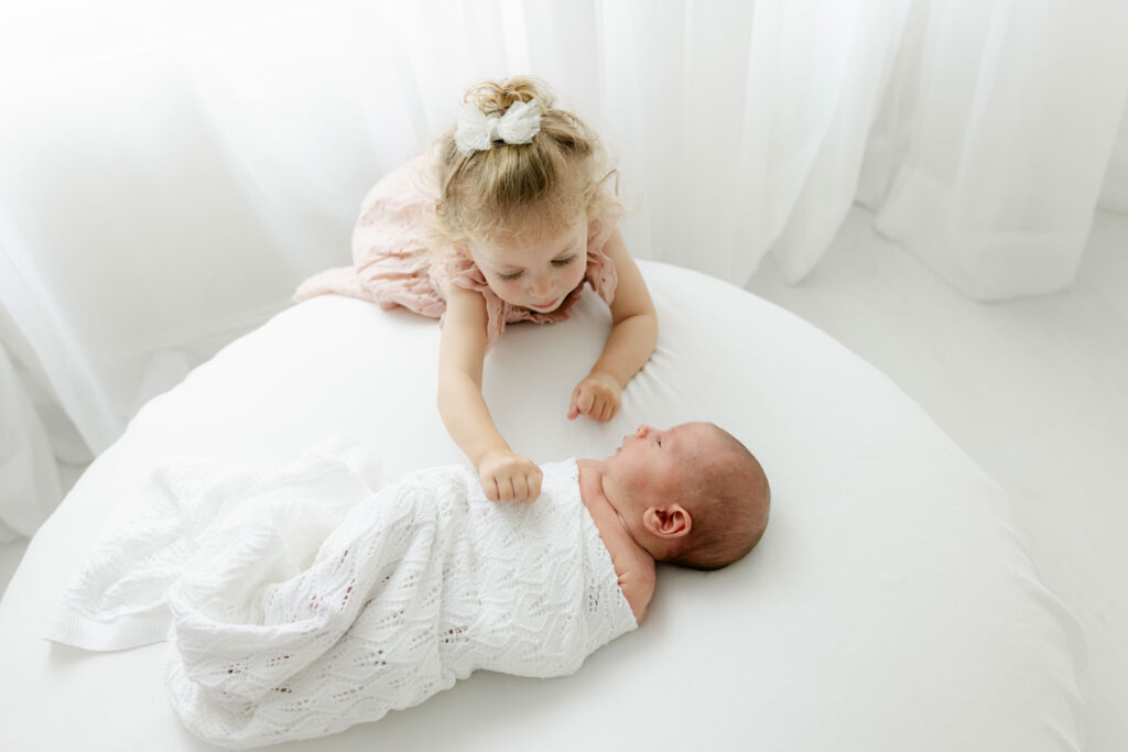 toddler girl touching her newborn brother