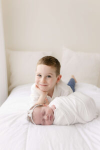little boy with newborn sister on a bed
